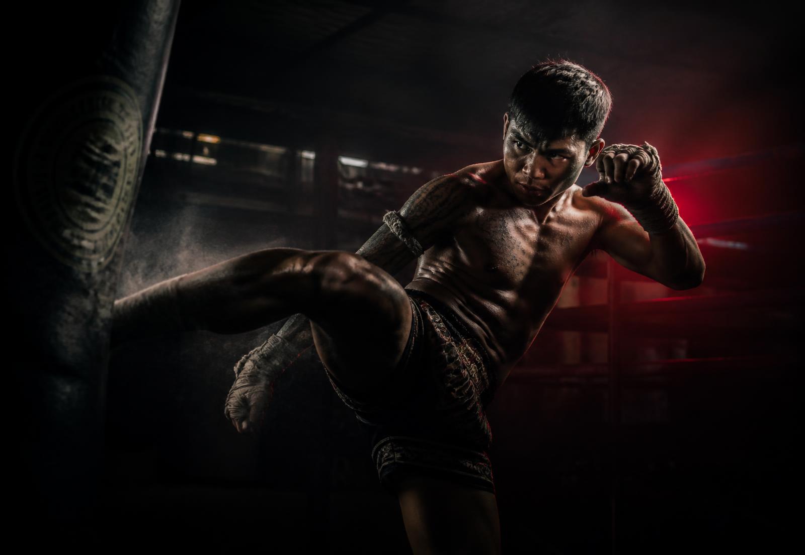 Muay Thai fighter striking a heavy bag in a dark training hall